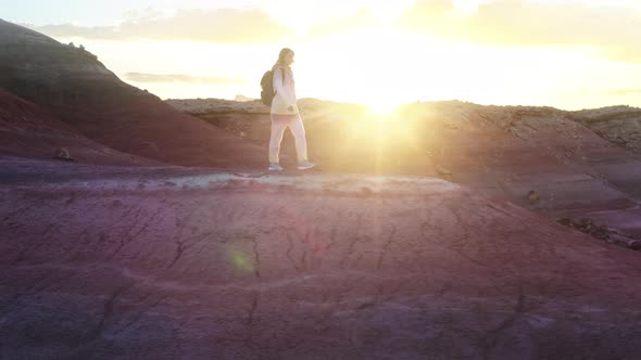Happy Woman Walking in Colorful Red Desert at Golden Sunset with Sun Rays Flare alt
