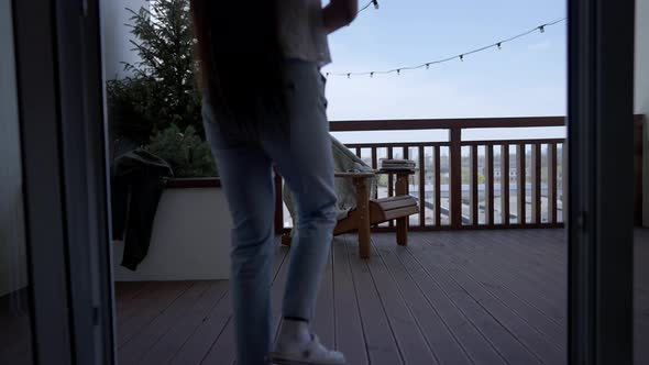 Slim Young Asian Woman Walking to Wooden Armchair on Deck Sitting Down and Opening Laptop alt