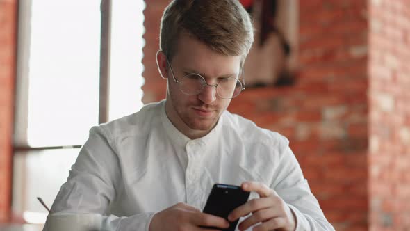 Attractive Man Glasses Standing Alone Indoor Holding in Hands Smart Phone Dial Number on Touchscreen alt