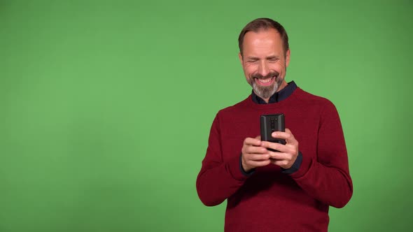 A Middleaged Handsome Caucasian Man Works on a Smartphone with a Smile  Green Screen Background