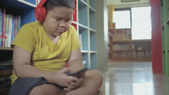 Asian little boy with red headphones using smartphone at home.