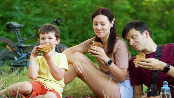 Parents and child enjoying picnic in nature after bike ride alt