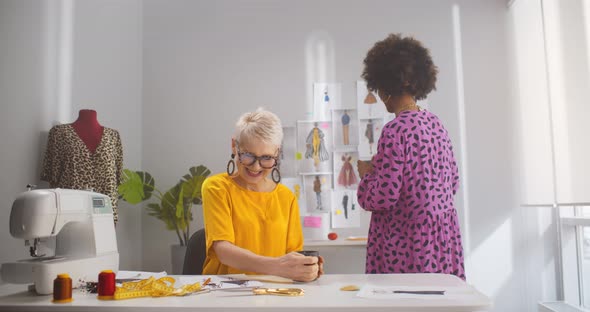 African Young Designer Bringing Coffee to Mature Colleague Working Together in Atelier alt