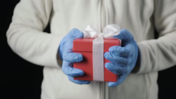 Little Girl's Hands in Blue Protective Gloves Giving Gift Box with White Ribbon