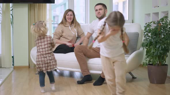 Happy Caucasian Woman Sitting on Couch Looking at Children Spinning in Slow Motion As Man Scolding alt