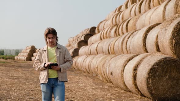 Farmer Agronomist Checks Hay Bales on the Wheat Field After Harvest at Sunset alt