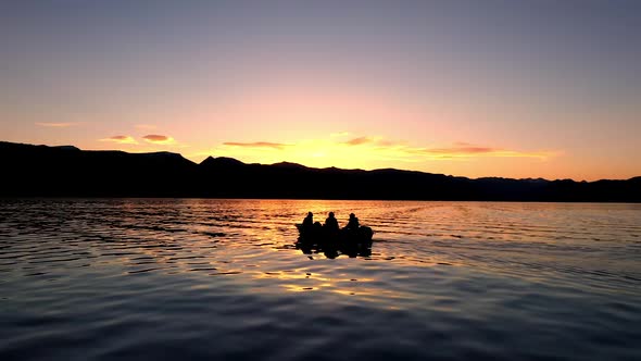 4 people fishing in a boat floating on a lake at sunset alt