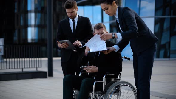 Businessman in a Wheelchair with Colleagues Outside an Office Building Discuss Abut Deal and alt