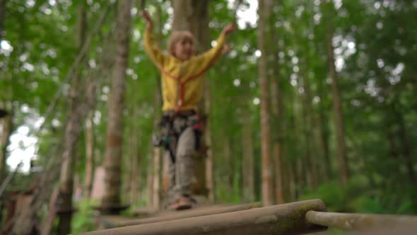 Superslowmotion Shot of a Little Boy in a Safety Harness Climbs on a Route in Treetops in a Forest alt