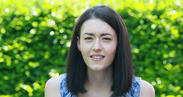 face portrait of young woman in a garden expressing mixed positive and negative emotions