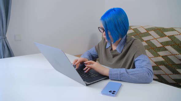White girl with blue hair working on laptop computer at home in 4k stock video clip alt