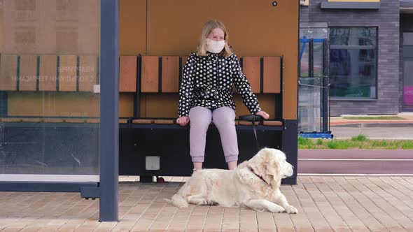 Coronavirus Pandemic in the City. Girl in a Protective Mask Sits at a Public Transport Stop