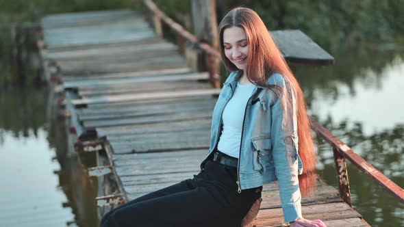 A Young Girl with Long Hair Poses By the Bridge on the River alt