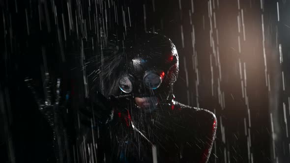 Woman in Latex Suit and Mask is Standing Under Water Flow in Studio Silhouette in Darkness alt