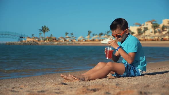 Attractive Teen Boy in Sunglasses Drinking Lemonade at Beach. Boy Putting Glass alt