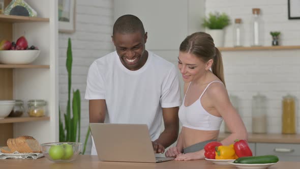 Athletic Woman and African Man Working on Laptop in Kitchen alt