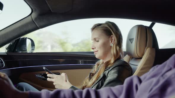 A female passenger typing on the phone is talking to the driver.