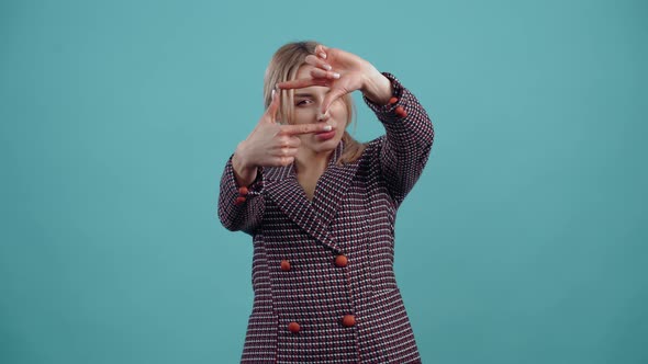 The Beautiful Young Blonde Puts Her Fingers in the Shape of a Picture and Looks Carefully Through It alt