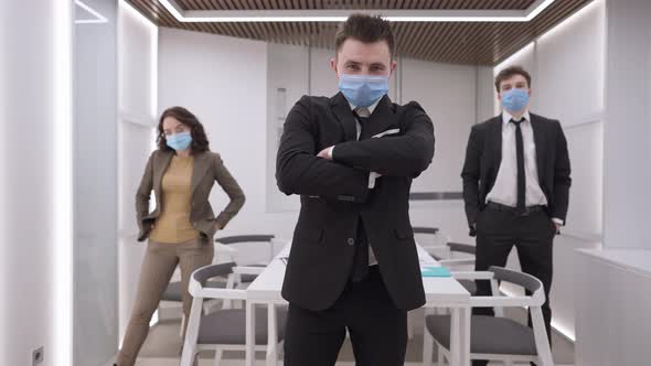 Portrait of Confident Caucasian Man Crossing Hands Looking at Camera with Blurred Colleagues in alt