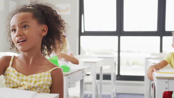 Video of happy diverse girls sitting at school desks and learning alt