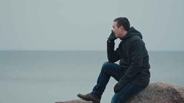 A young guy is sitting on a stone against the background of the blue sea