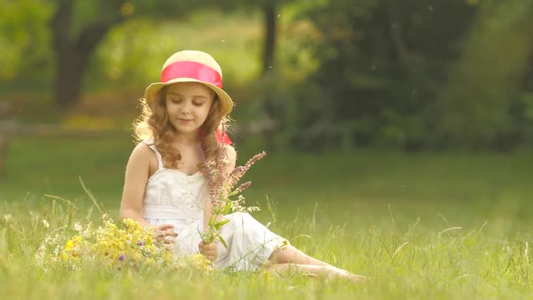 Little Girl Sits in a Clearing, Turns Over the Torn Wild Flowers and Makes a Bouquet From Them alt