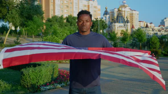 Portrait Afroamerican Man Holding an American Flag and Looks Camera in Summer alt