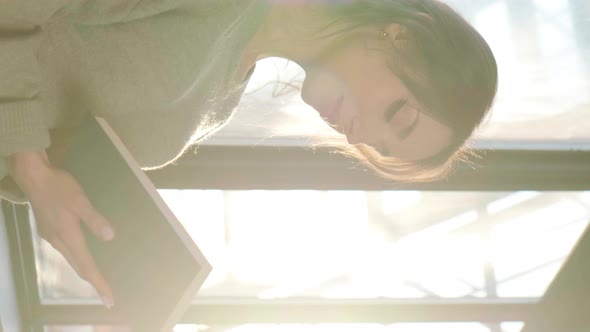 Beautiful Woman Sitting Near Window and Reading a Book on Background of Sunset alt