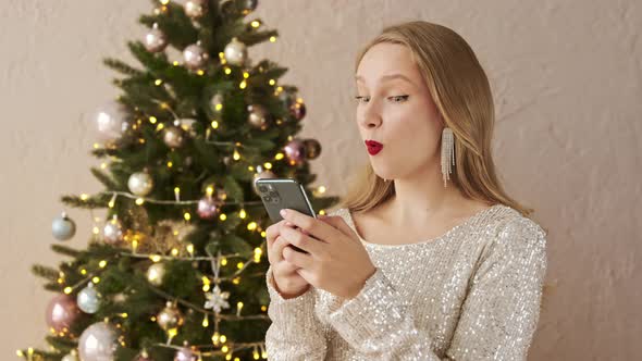 Amazed christmas woman using mobile phone, sees message with a good news or gossip and says wow. alt