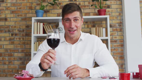 Caucasian man making video call drinking glass of red wine and talking alt