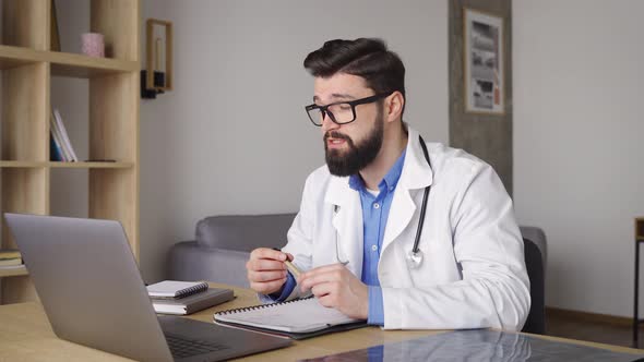 Male Doctor in White Coat with Stethoscope Using Laptop for Online Consultation
