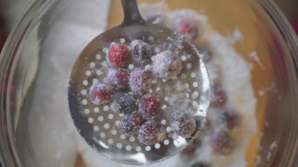 Slow motion close up view of sugar and cranberries sifting and being coated in clear glass bowl on w alt