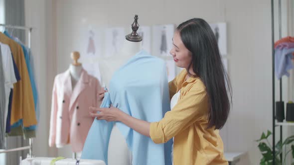 Smiling Asian Female Designer Wearing Fabric On A Mannequin While Designing Clothes In The Studio alt