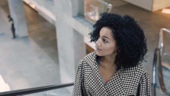 Stylish African American Woman in a Stylish Coat Climbs the Escalator in the Mall alt