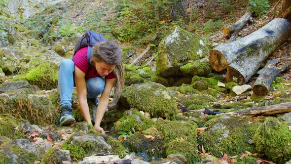 Young Woman Quenches Thirst Near Forest Brook alt