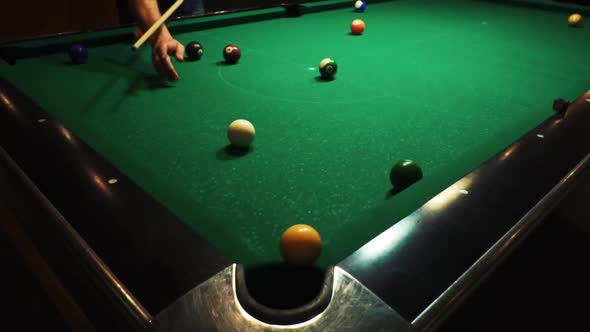 Man plays pool in dark bar, hits ball with cue, ball hit the pocket. Playing billiard on green table