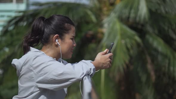 Smiling portrait beautiful young Asian woman fitness runner standing using mobile phone.