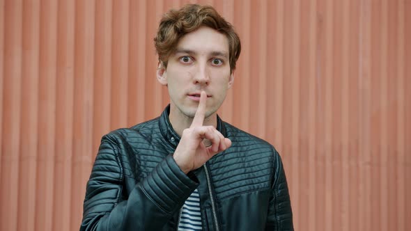 Emotional Young Man Making Shush Gesture Asking for Silence Standing Outdoors alt