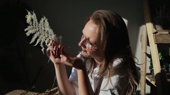 A Woman with a Fern Looks Through It at the Sun While at Home