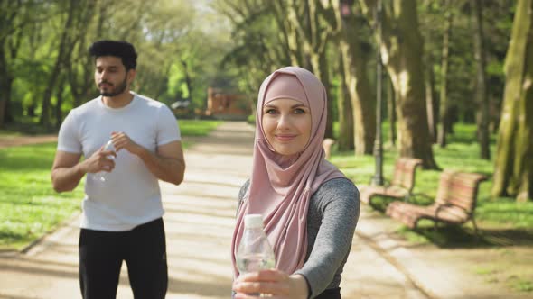 Pretty Woman in Hijab Holding Water of Bottle While Muslim Guy Standing Behind alt