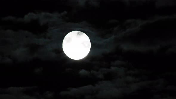 Moon time lapse as it rises into the night sky. Moon rising with clouds passing by for a spooky, eer alt