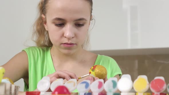 A Girl is Concentrating on Drawing a Picture on an Easter Egg with Yellow Paint