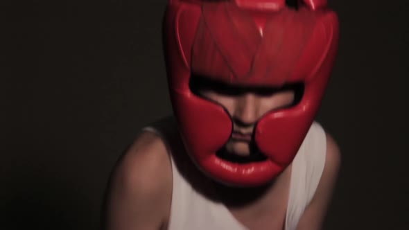 Young guy boxer in a red protective helmet posing at the camera close-up in bandages