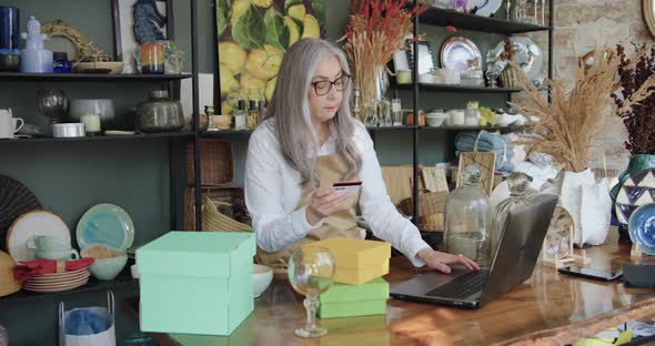 Female Seller sitting in Souvenir Shop and Entering Bank Card Details Into Computer alt