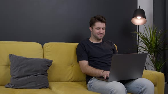 Young Unshaven Handsome Guy Chatting Messaging Online Sitting on Sofa Copy Space