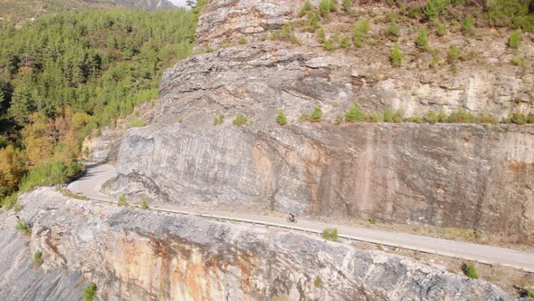 Cyclist going down serpentine road in mountain woods. alt