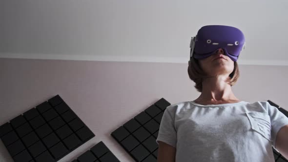 Young Woman in a VR Helmet Plays a Game at Home alt