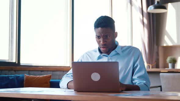 Portrait of frustrated young businessman looking at laptop in kitchen alt