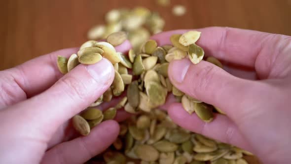 A Lot of Raw Pumpkin Seeds Fall From Female Hands on the Table alt