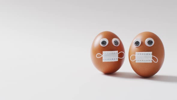 Video of eggs with eyes and face masks on a white surface alt
